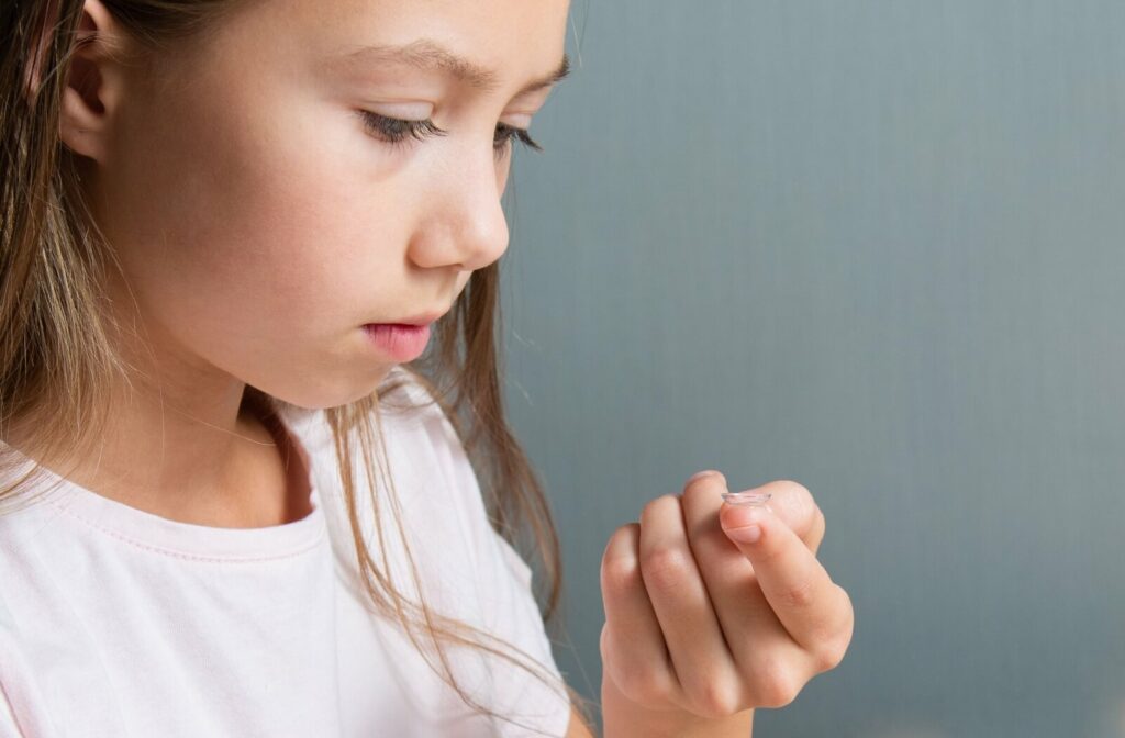 A near shot of a little girl looking at a contact lens for myopia on her index finger.