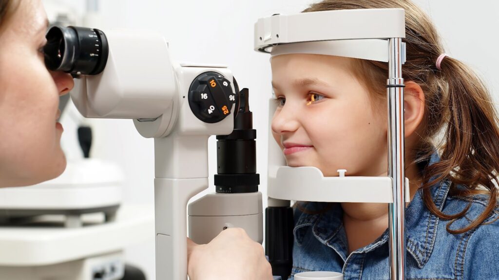 An optometrist uses a slit lamp to examine a child's eye.