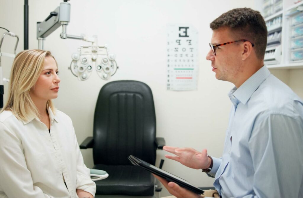 Optometrist explaining to a patient during an eye exam, both sitting in an examination room.
