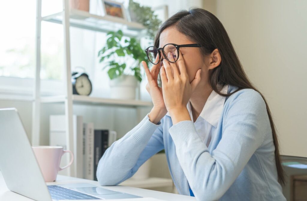 A woman sitting at a computer, experiencing dry eye symptoms that are causing blurry vision.