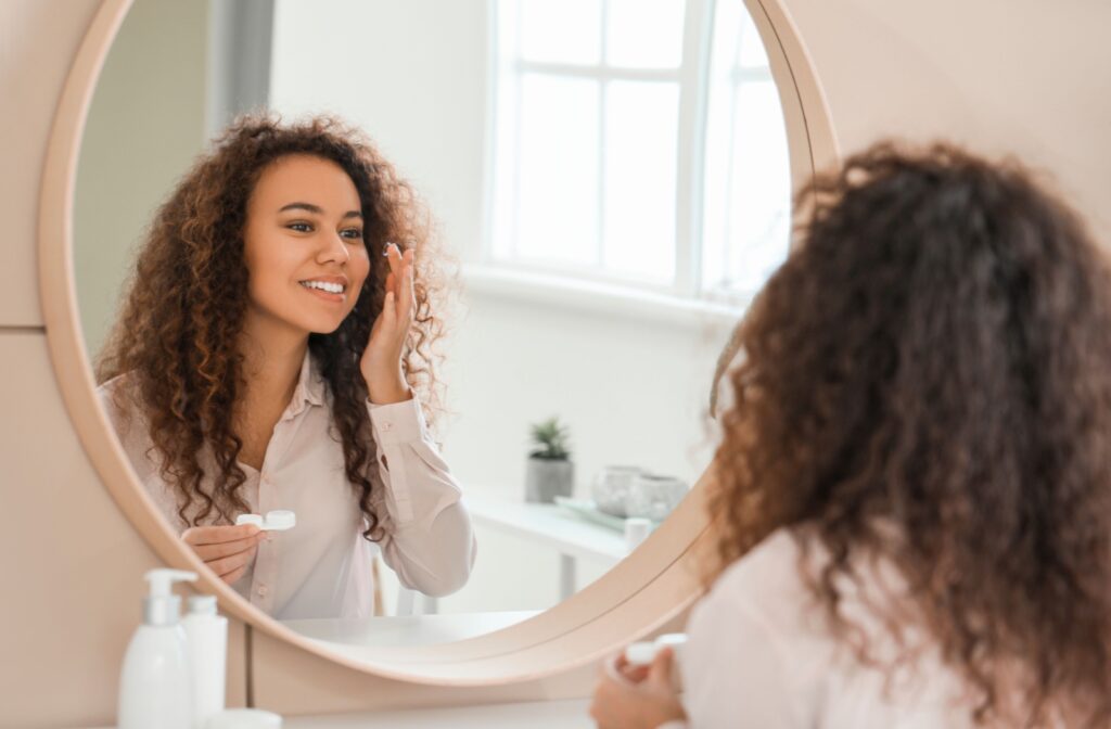 An adult concentrates as they look in the mirror to insert their contact lens.