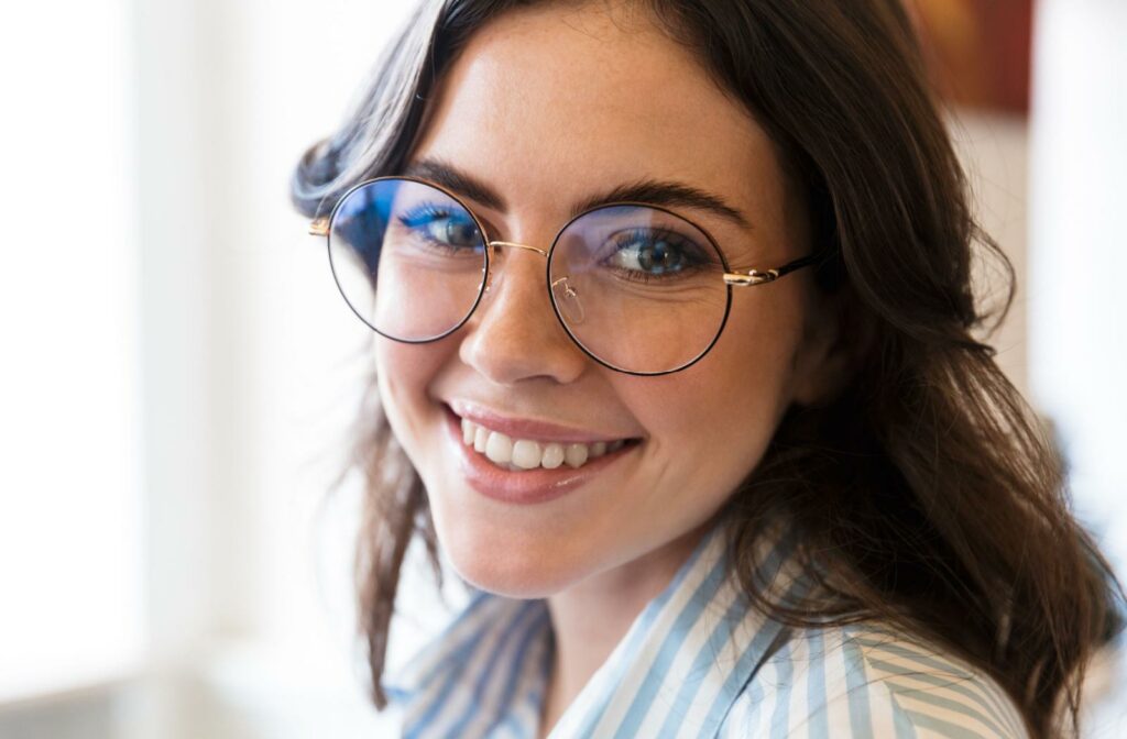 A close up of a person smiling face while they wear a pair of thin-framed glasses